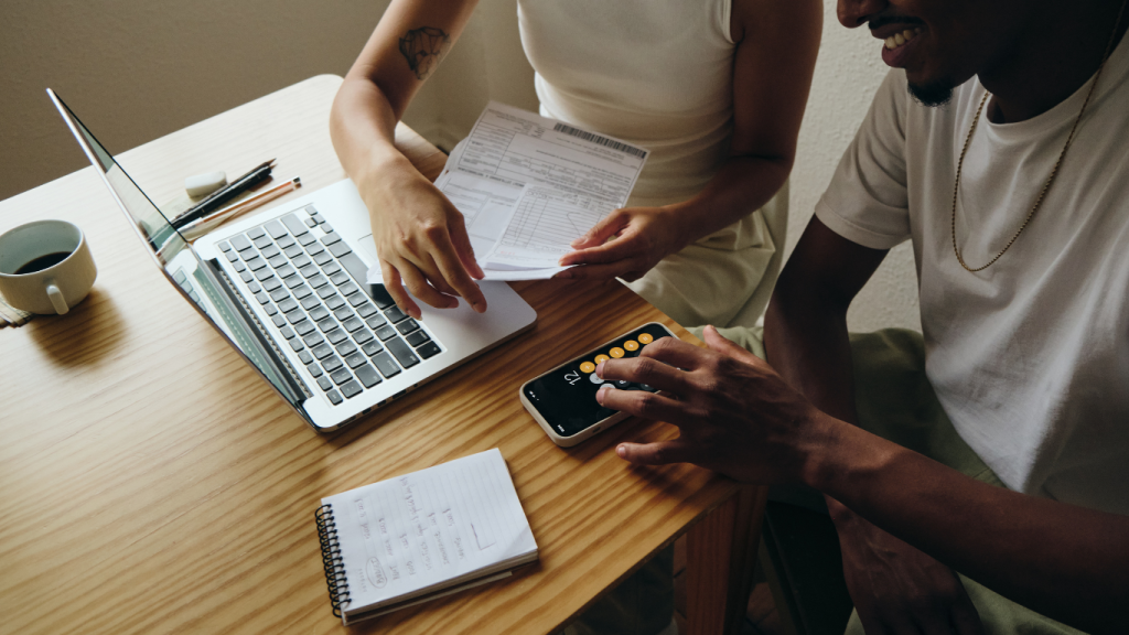 Casal com calculadora, e boletos sentados em uma mesa.