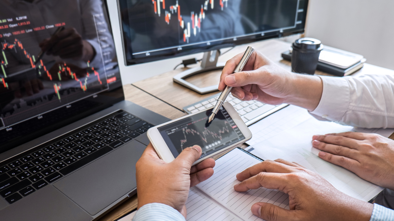 Dois homens vendo sobre investimentos no computador e celular.