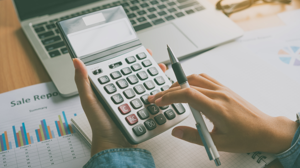 Mulher na calculadora, com notebook e papéis na mesa.