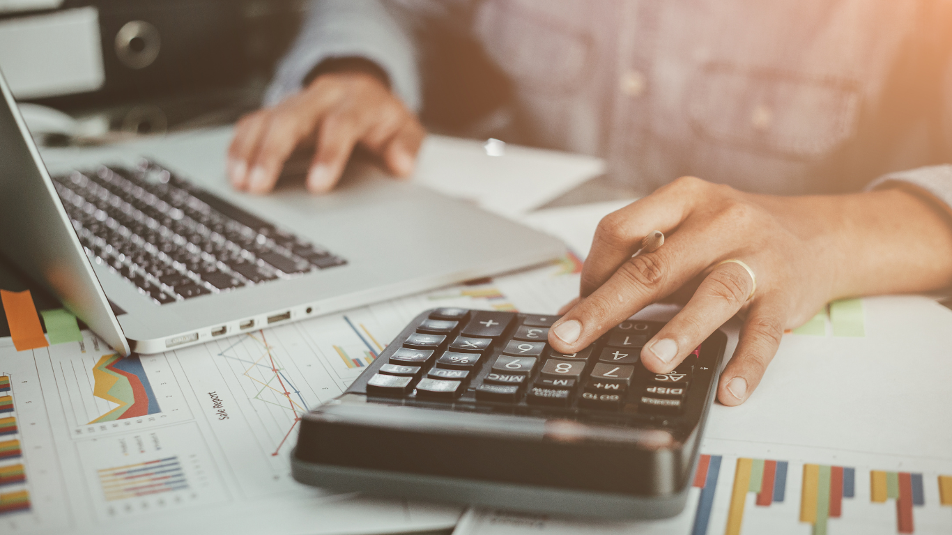 Homem sentado em uma mesa com calculadora e notebook.