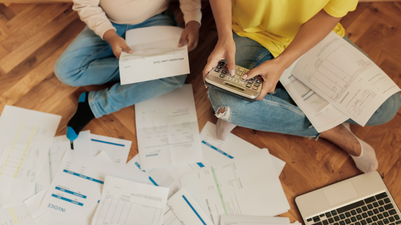 Duas pessoas sentadas com vários boletos e calculadora na mão.